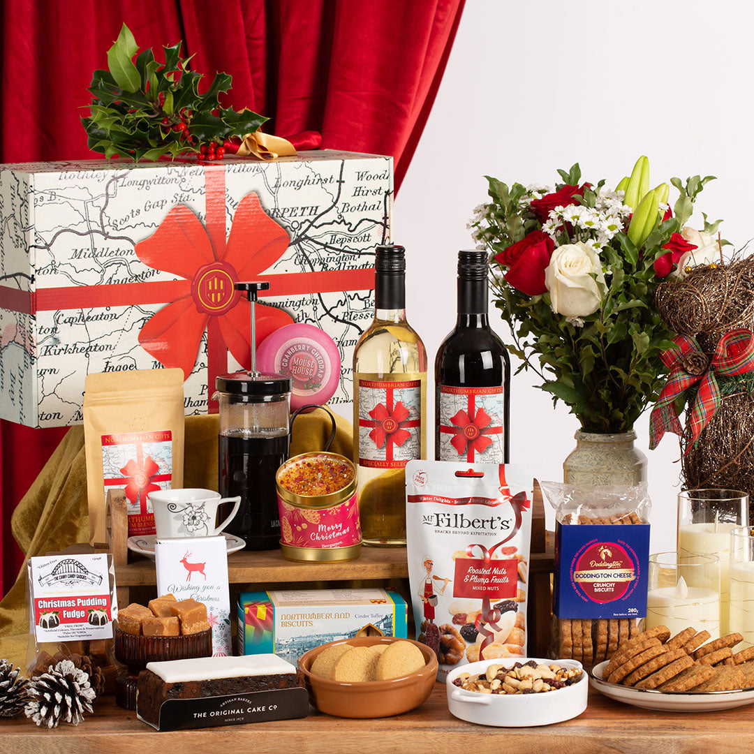 Gourmet gift basket with wine, coffee, snacks, and a decorative box on a wooden table.